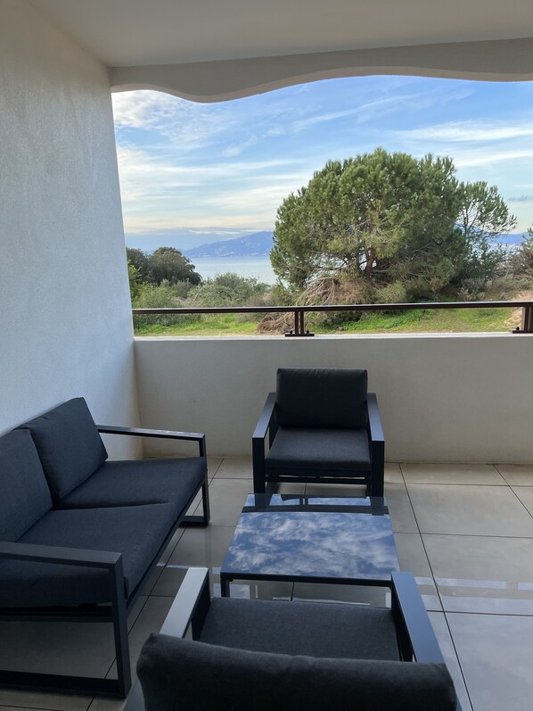 A balcony with two dark-colored sofas and a small table, overlooking a coastal landscape with trees and a view of the sea. - Loc a Machja Fiurita 2 (Pietrosella)