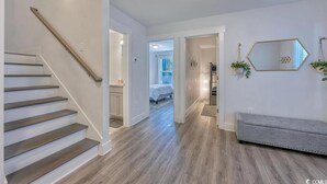 Un intérieur moderne avec un escalier en bois, un couloir menant à une chambre, et un coin salon avec un banc.