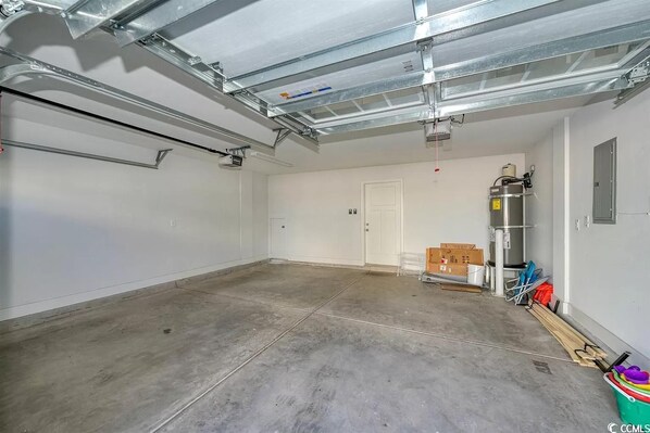 A spacious, empty garage with a concrete floor, white walls, and a door. - Beautiful new home, 3 Bed 2.5 bath, 4min walk to beach (Myrtle Beach)