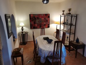 Un coin repas avec une table dressée pour deux personnes, une étagère murale ornée d’objets décoratifs et un tableau encadré accroché au mur.