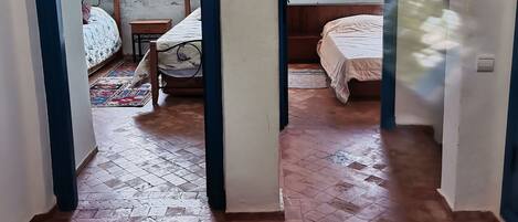 A room with two beds, a small table, and a view through an archway.