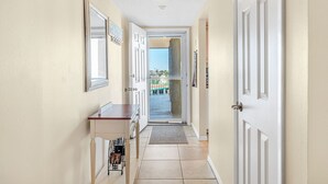 A hallway with a door leading to a balcony, a small table, and a wall-mounted mirror. - ⛱️ PENTHOUSE VIEWS 🚀🌴👙 (Cocoa Beach)