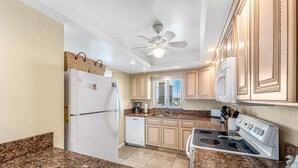 A kitchen with granite countertops, a white refrigerator, a dishwasher, a stove, and wooden cabinets. - ⛱️ PENTHOUSE VIEWS 🚀🌴👙 (Cocoa Beach)