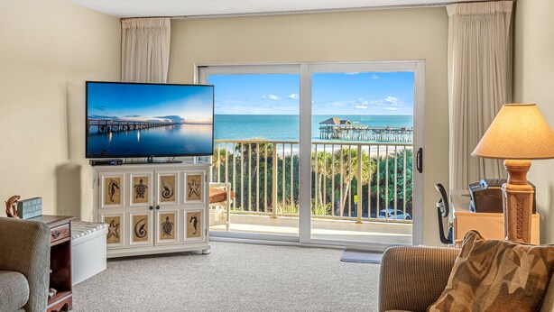 A hotel room with a large TV, a balcony with a view of the sea, and a wooden cabinet with decorative starfish. - ⛱️ PENTHOUSE VIEWS 🚀🌴👙 (Cocoa Beach)