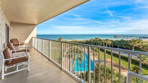 A balcony with white chairs, a pool, and a view of the beach and pier. - ⛱️ PENTHOUSE VIEWS 🚀🌴👙 (Cocoa Beach)