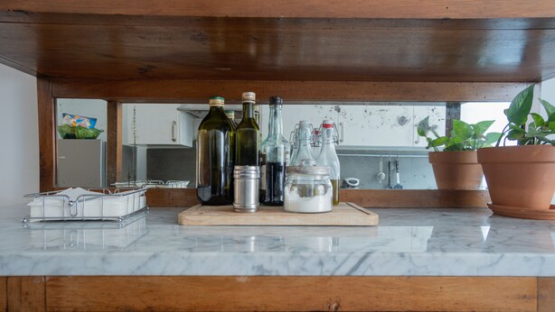 A kitchen counter with various bottles, a cutting board, and potted plants.