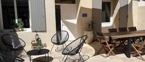 Un espace extérieur aménagé avec des chaises et une table, un pot de fleurs et l’entrée d’un bâtiment.