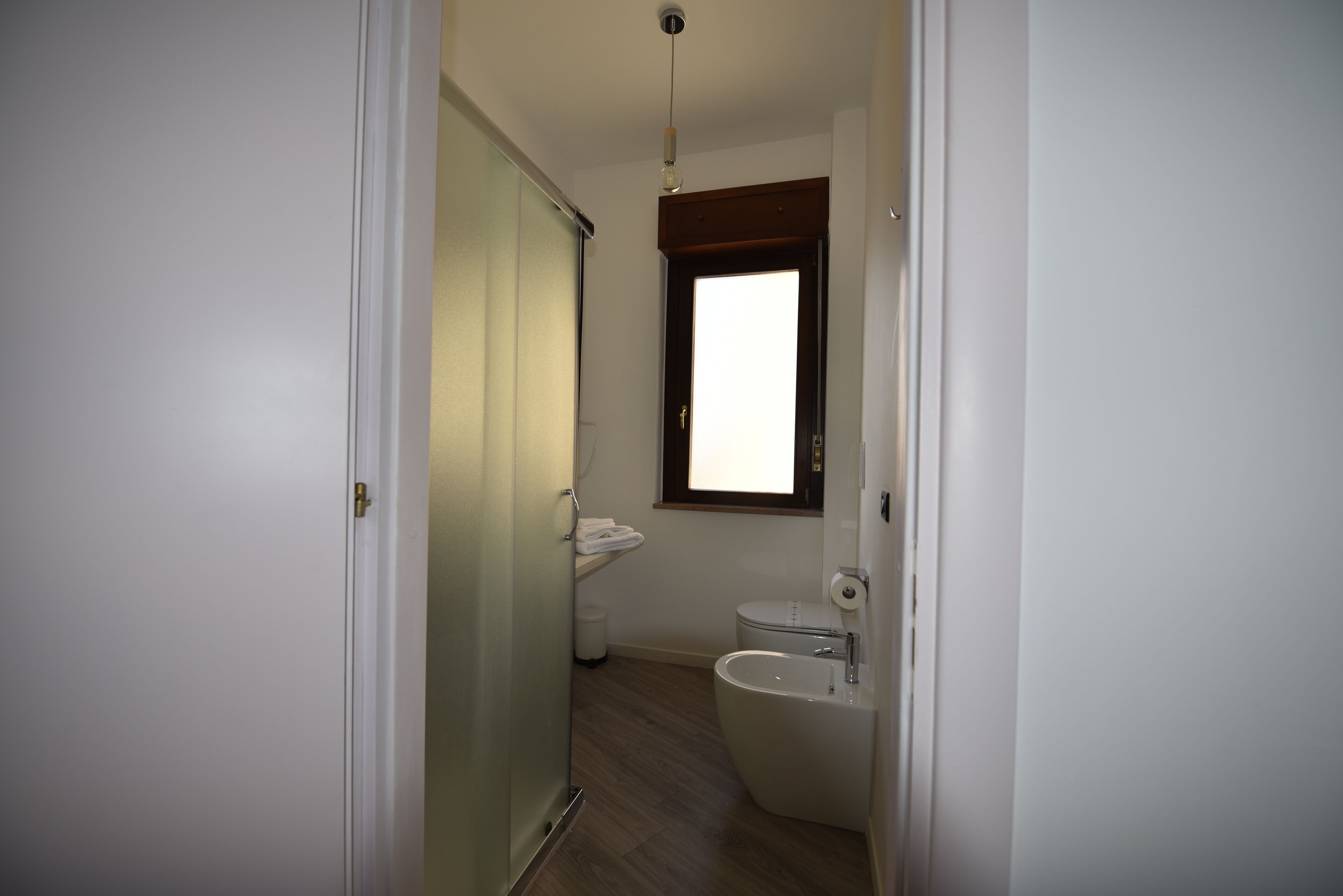 A small, clean bathroom with a toilet, bidet, and a window providing natural light.