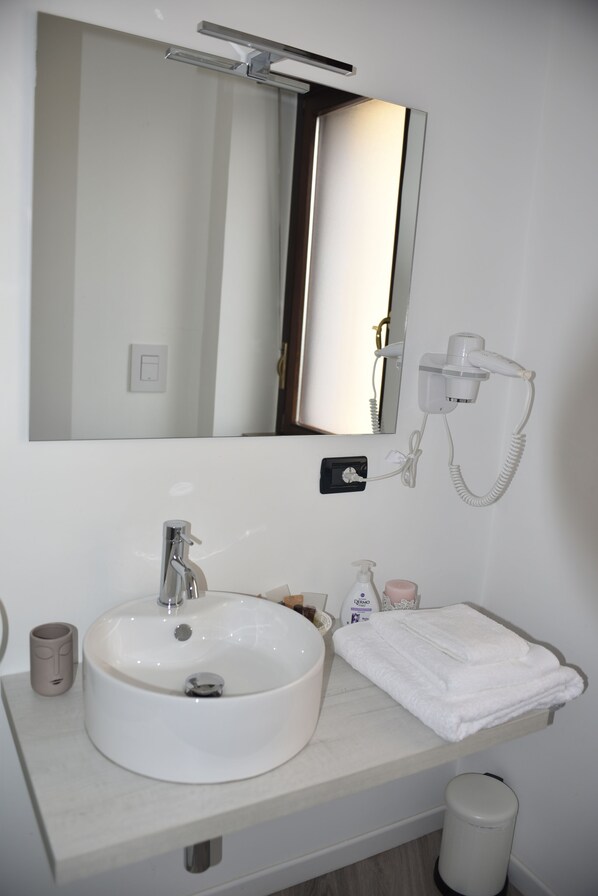 Un baño con lavamanos blanco, un espejo, un secador de pelo y una toalla.