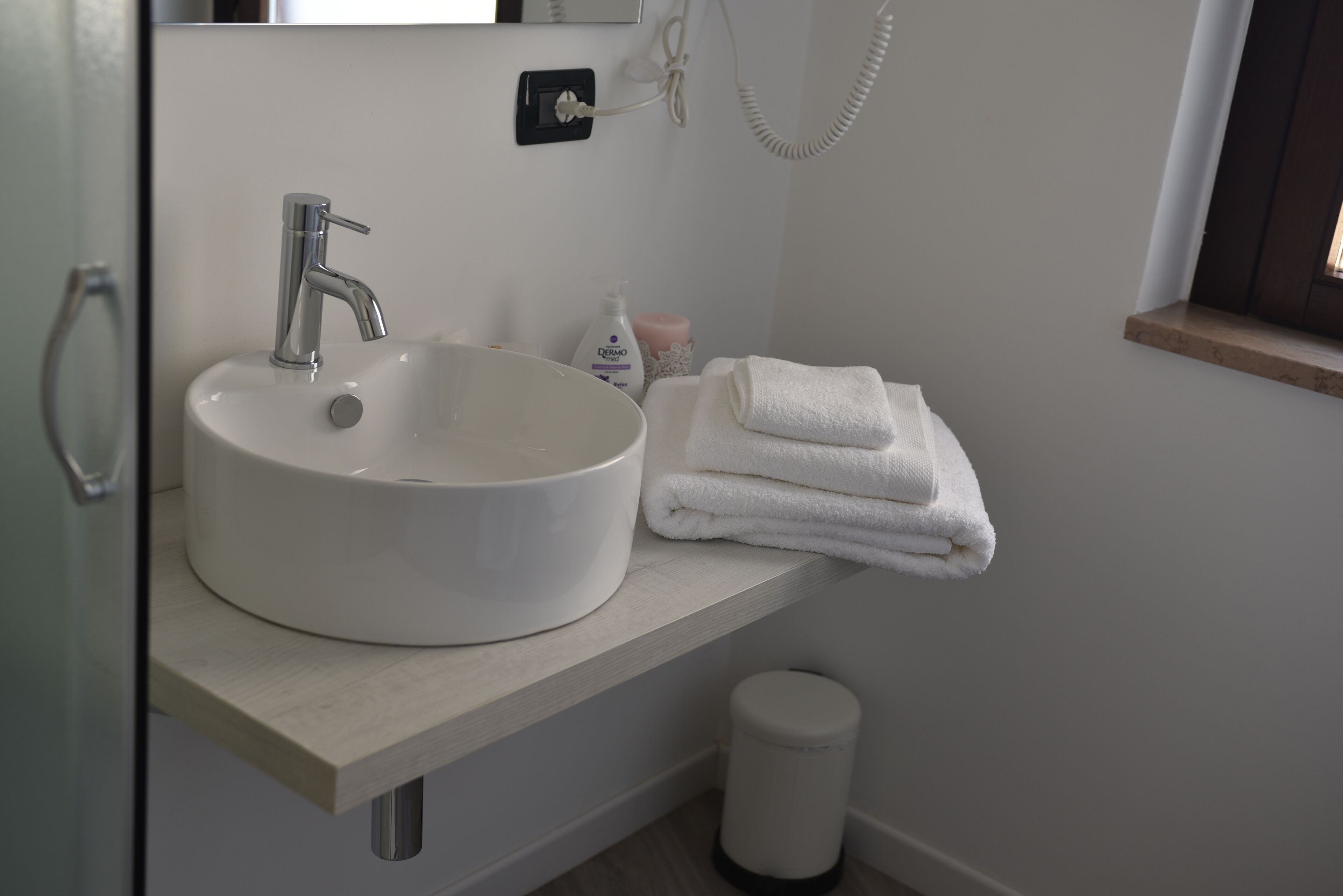 A bathroom with a white sink, a towel rack, and a trash bin.
