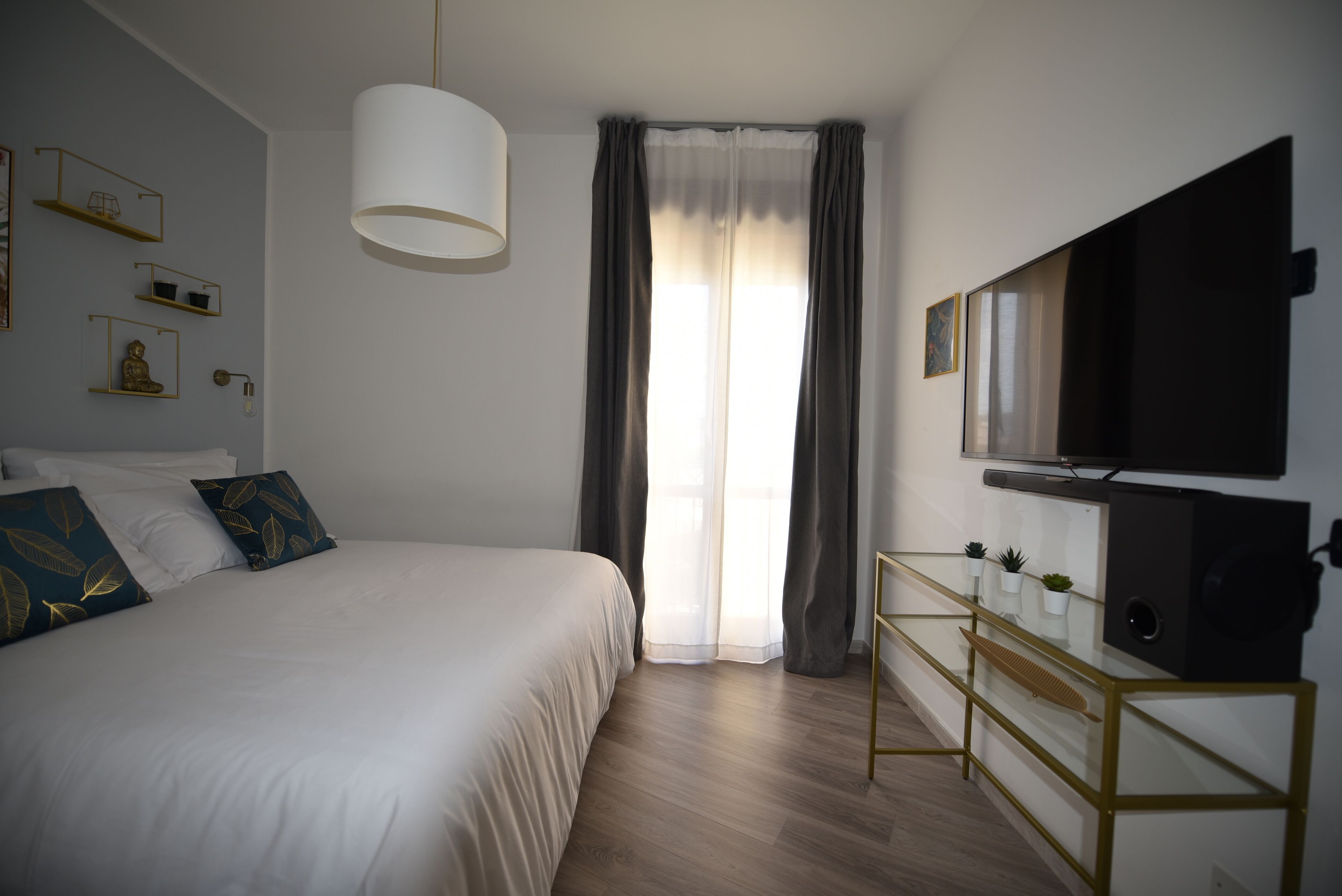 A bedroom with a bed, a bedside table, a TV, and a window with curtains.