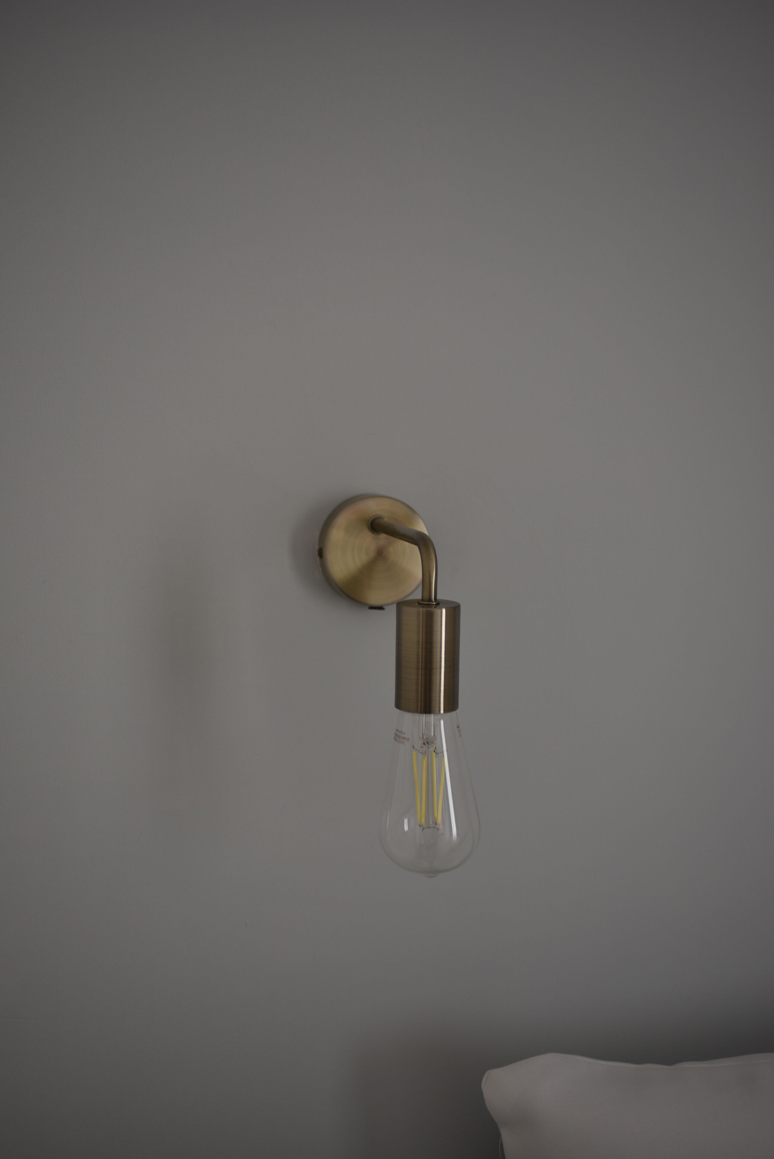A wall-mounted light fixture with a clear glass bulb and a metallic base.