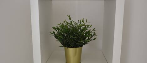 A white shelving unit with three gold-colored pots containing green plants.