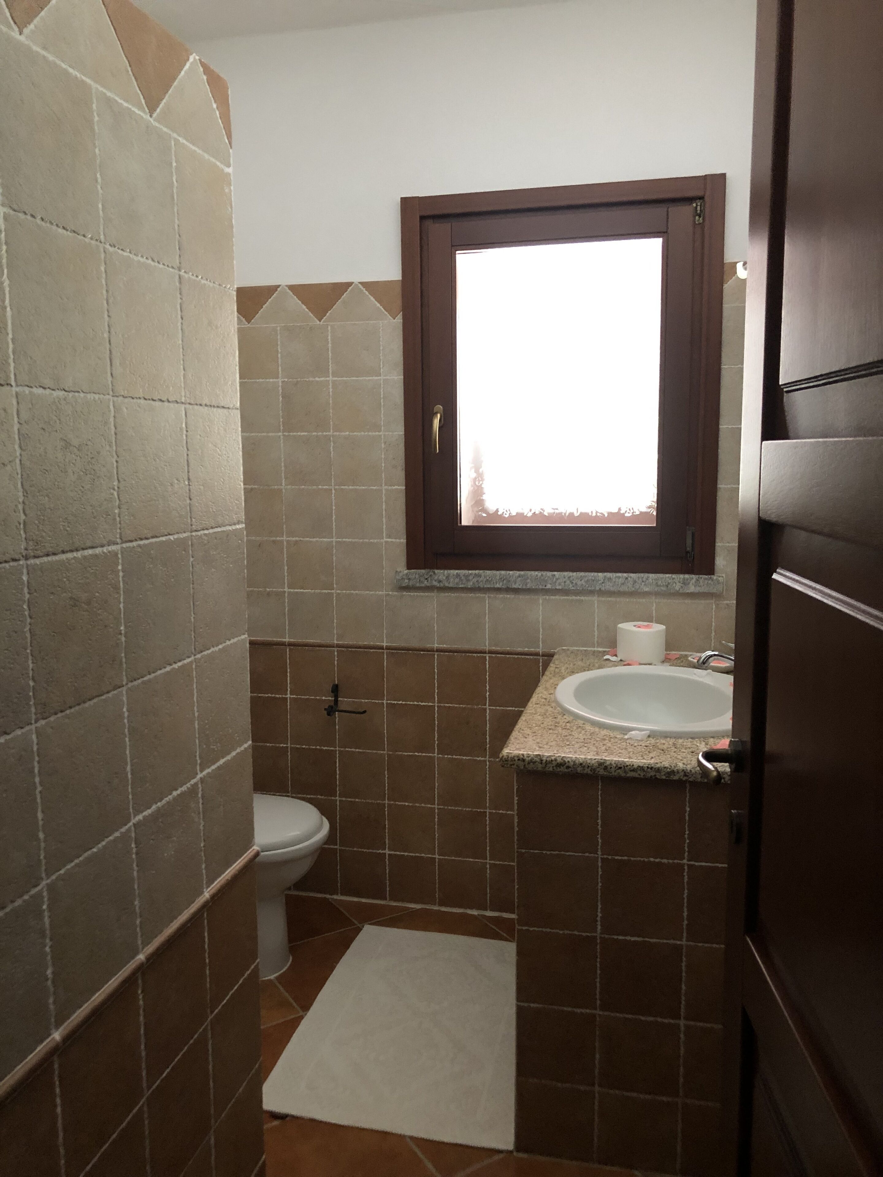 A small bathroom with a toilet, sink, and window.