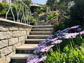 Eine Steintreppe mit Metallgeländer, umgeben von üppigem Grün und Blumen.