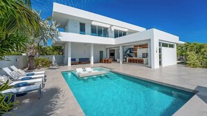 Une maison moderne à deux étages, dotée d’une piscine, d’un espace de détente extérieur et d’un escalier menant à l’étage supérieur.