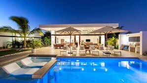 A modern pool area with lounge chairs and umbrellas, a dining area with tables and chairs, and a large house in the background. - Great for Friends/Families, Private Villa w/Pool 9 (Providenciales)