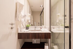 A modern bathroom with a wooden vanity, a glass shower enclosure, and a white towel hanging on the wall.