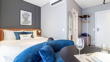 Una camera d'albergo moderna con un letto, un divano blu, un tavolo da pranzo con un bicchiere di vino e uno specchio.