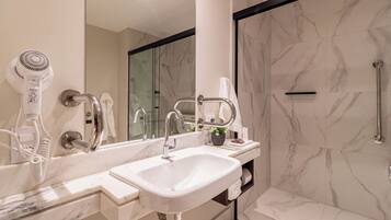 A modern bathroom with a large mirror, a white sink, a hairdryer, and a shower area.