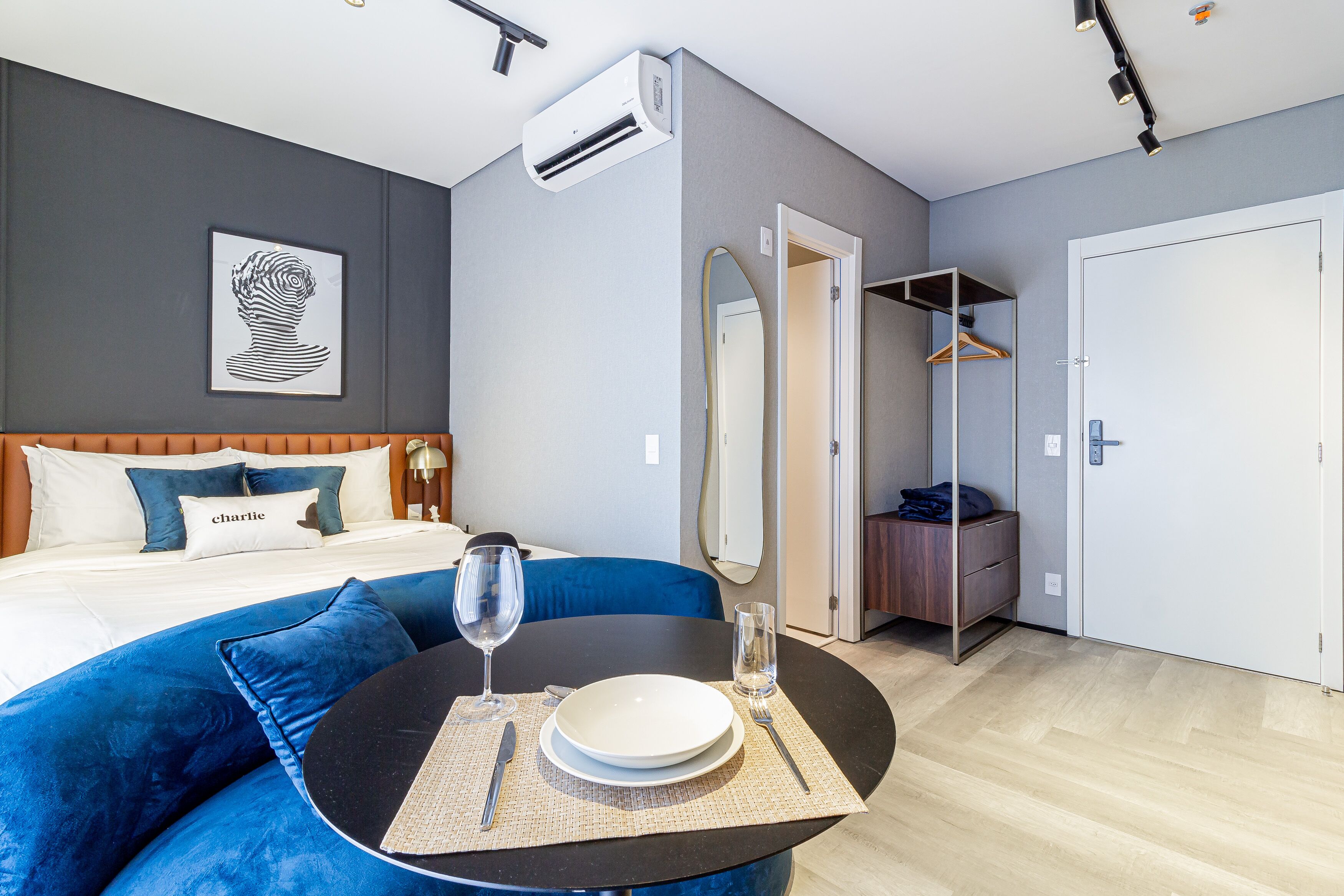 Una habitación de hotel moderna con cama, sofá azul, mesa de comedor con plato y cubiertos, y un armario.