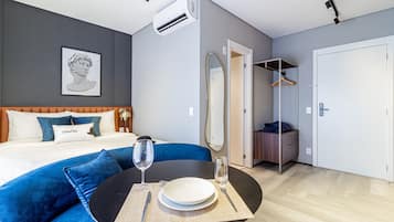 Una habitación de hotel moderna con cama, sofá azul, mesa de comedor con plato y cubiertos, y un armario.