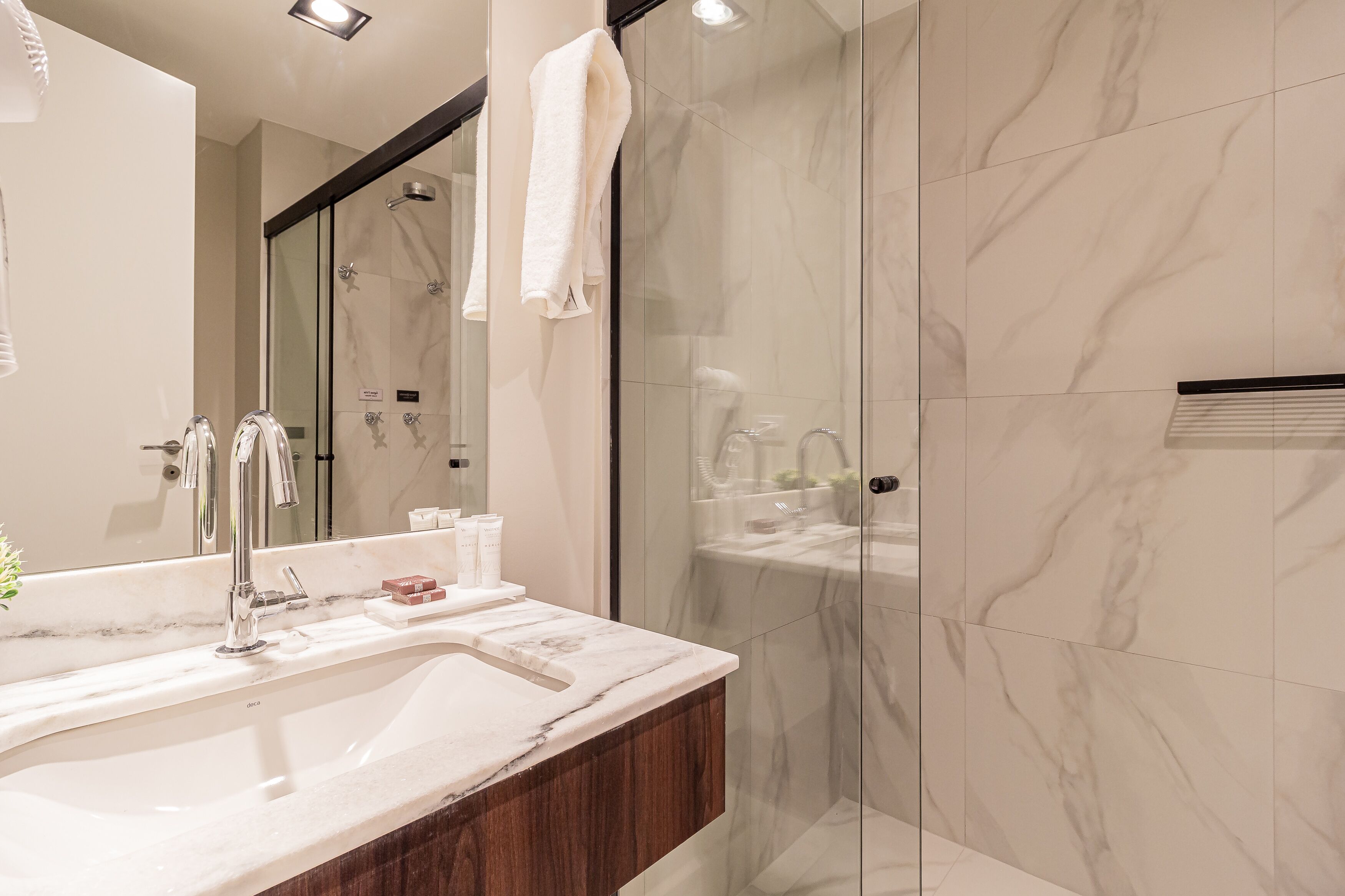 A modern bathroom with a marble sink, a glass shower enclosure, and a large mirror.