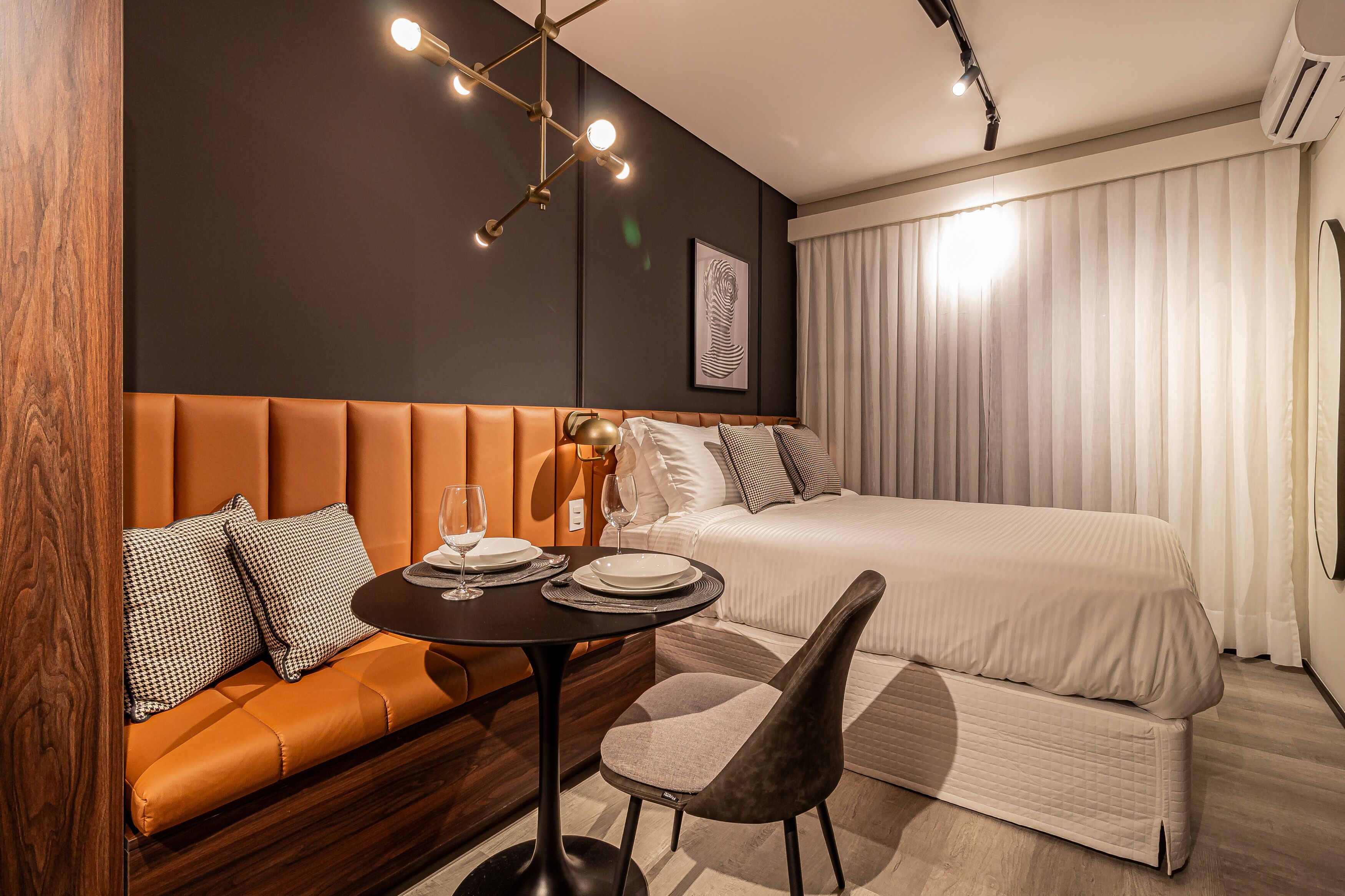 Quarto de hotel moderno com uma cama grande, um sofá, uma mesinha com copos e pratos, e um lustre de design único.