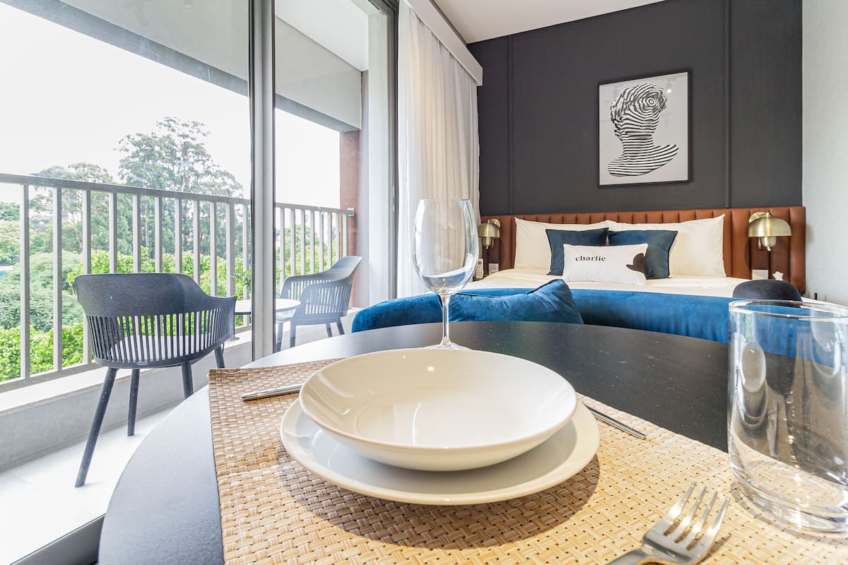 A hotel room with a balcony, a bed with blue and white bedding, and a dining table set with a plate, bowl, and glass.