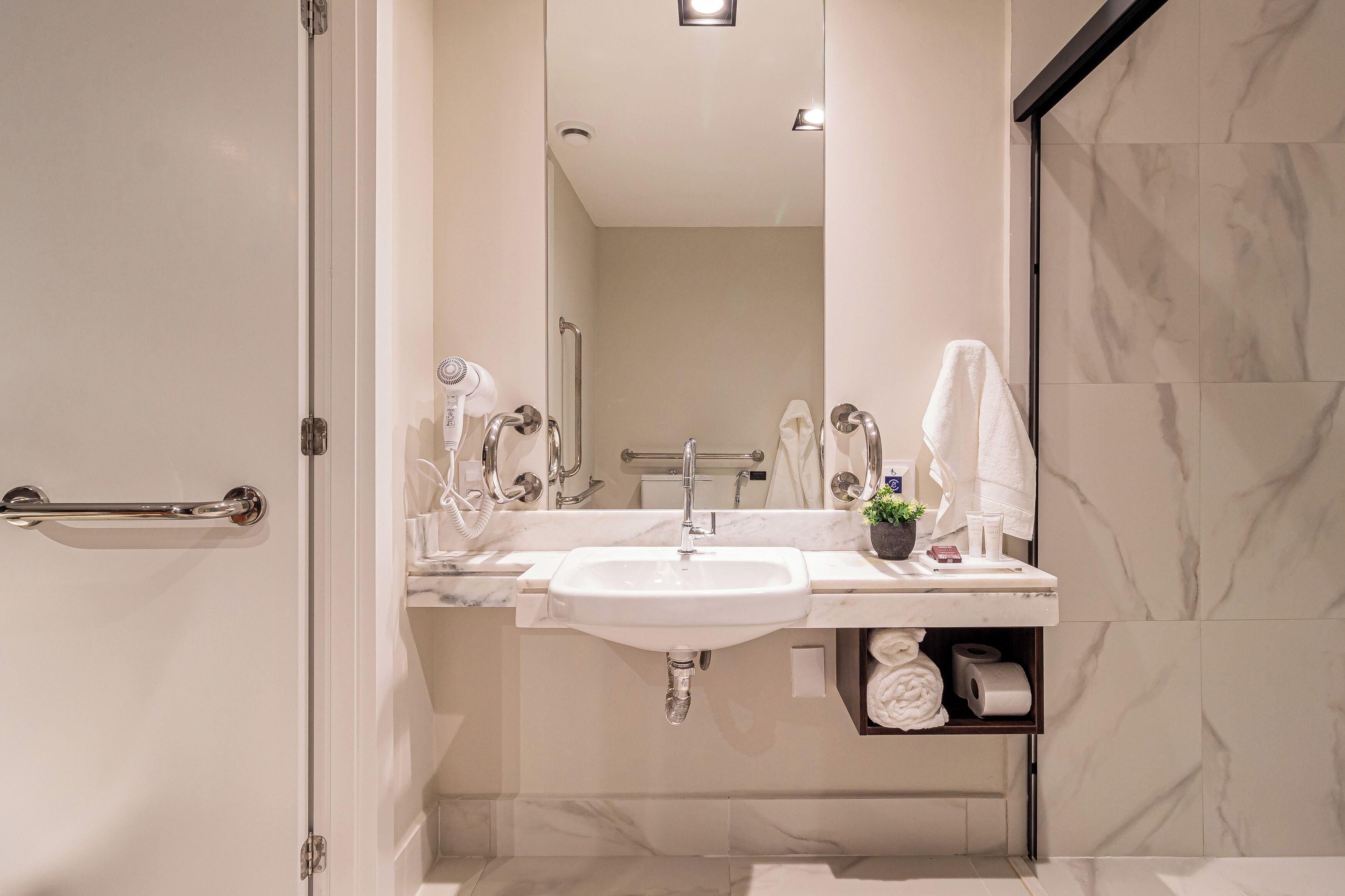 A modern bathroom with a white sink, a mirror, a towel rack, and a shelf with toiletries.
