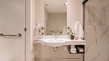 A modern bathroom with a white sink, a mirror, a towel rack, and a shelf with toiletries.