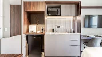 Una cocina compacta con microondas, lavamanos y un refrigerador pequeño.