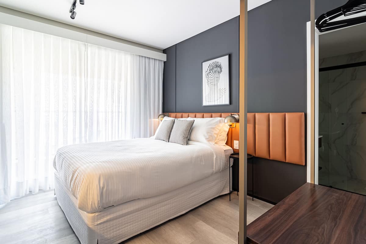 A modern hotel room with a large bed, a headboard with orange panels, a framed artwork on the wall, and a wooden floor.