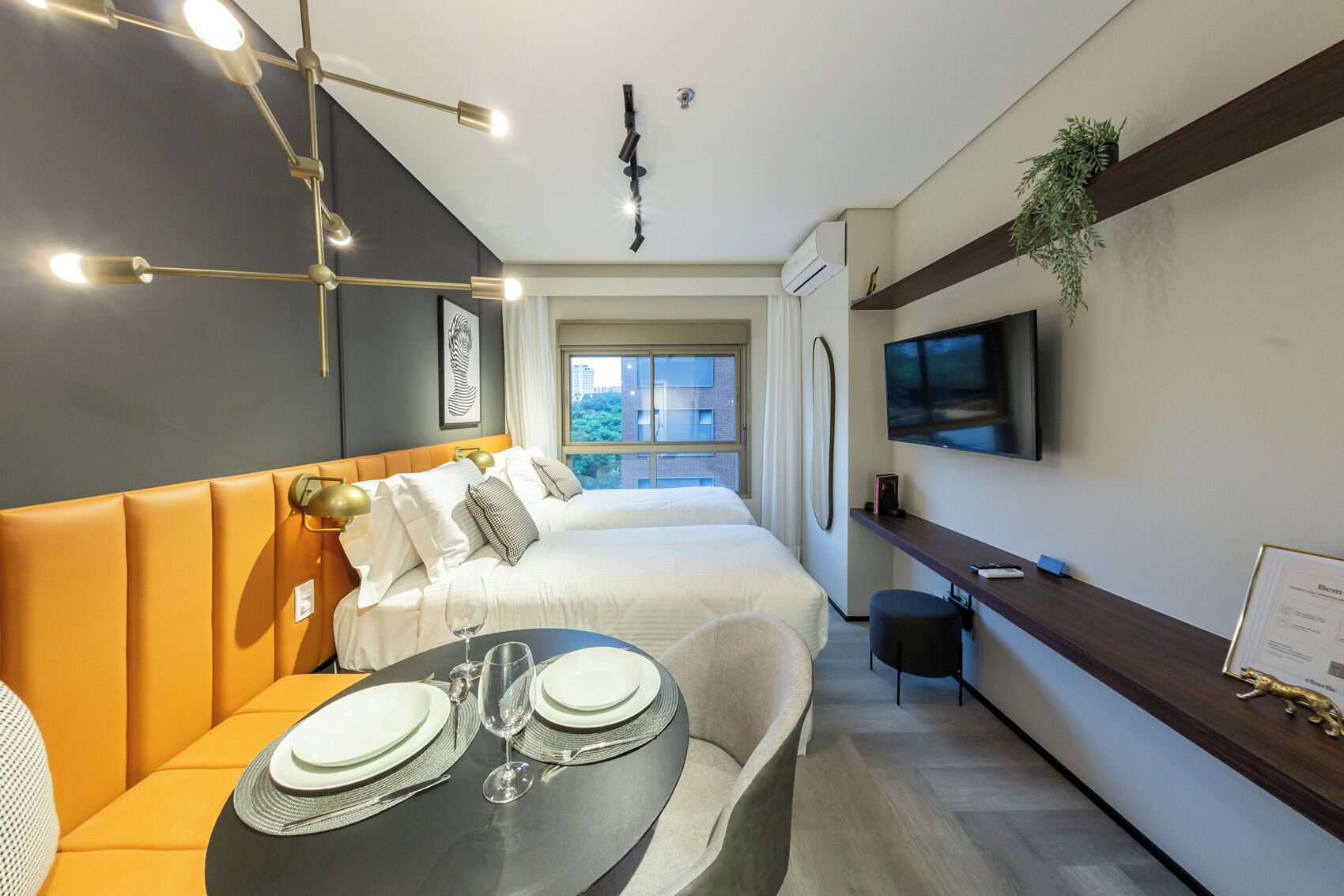 Ein modernes Hotelzimmer mit einem Bett, einer Couch, einem Esstisch für zwei Personen, einem an der Wand montierten Fernseher und einem Fenster mit Blick auf die Stadt.