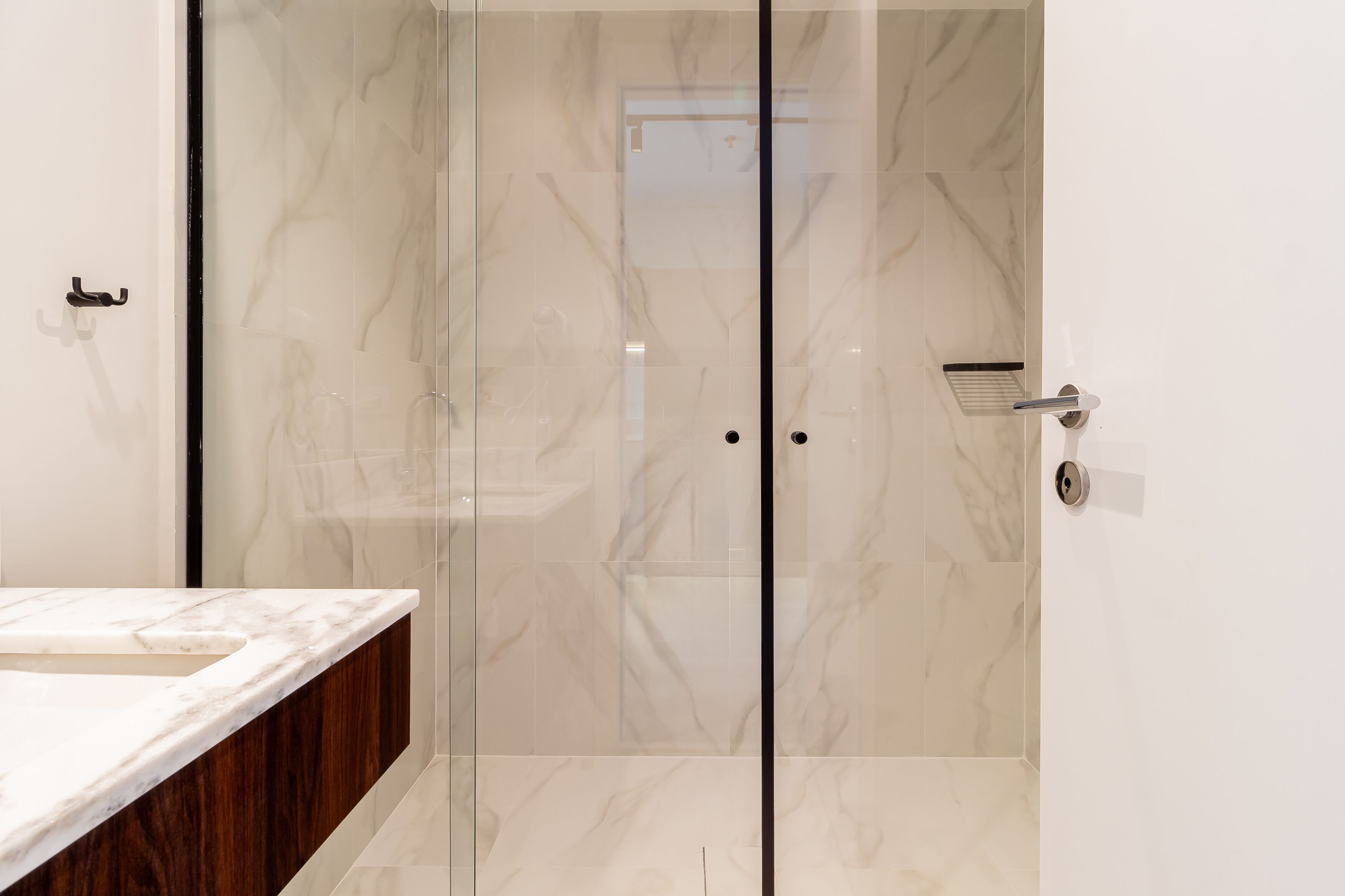 Une salle de bain avec une douche à l’italienne en marbre, un meuble-lavabo en bois et un lavabo blanc.