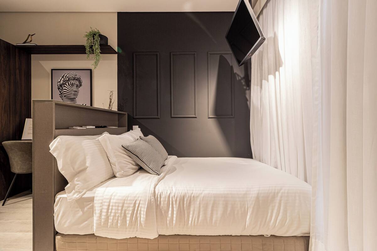 A modern bedroom with a bed, a desk, and a TV.