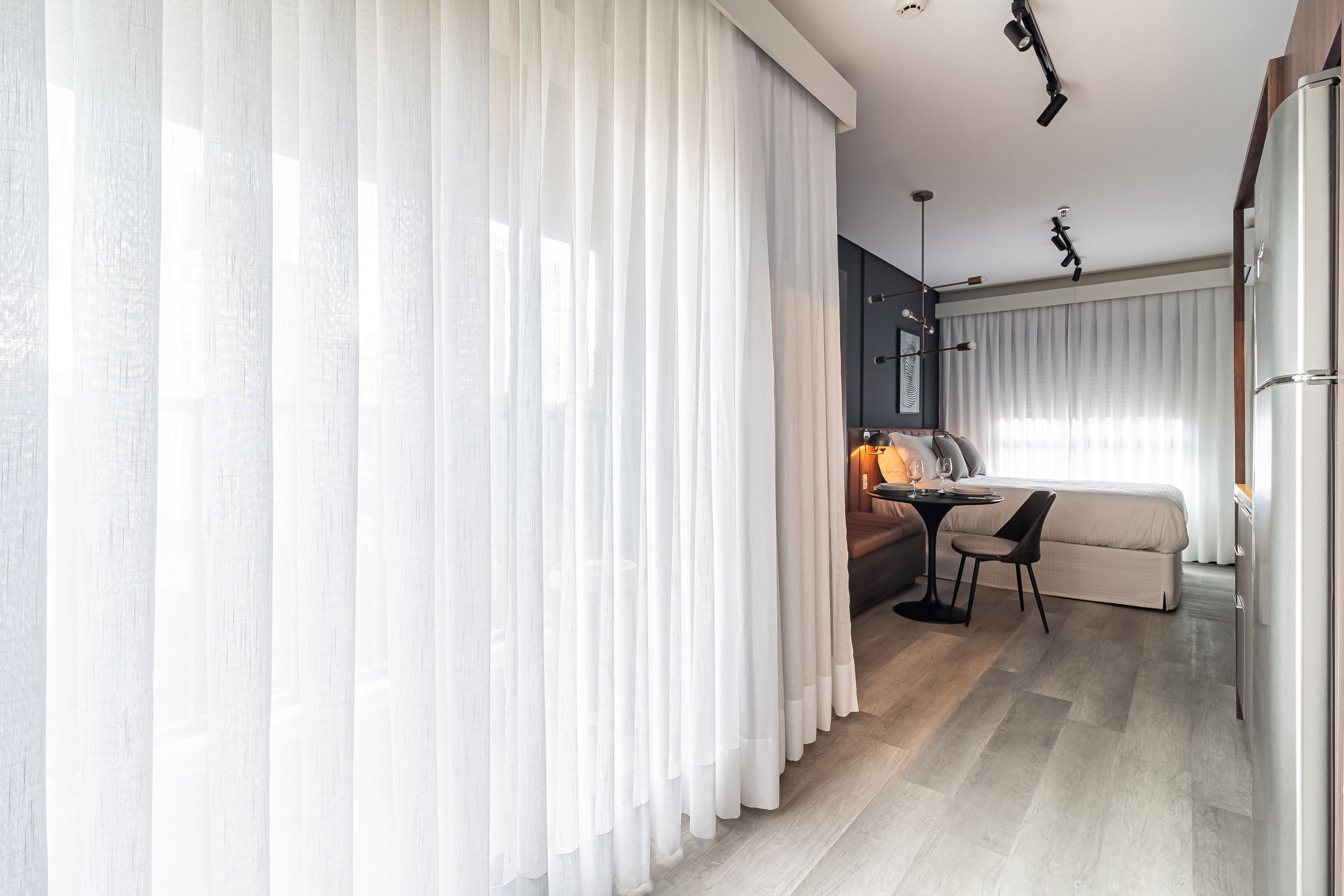 Een moderne hotelkamer met een groot raam, een bank, een eettafel en een kitchenette.