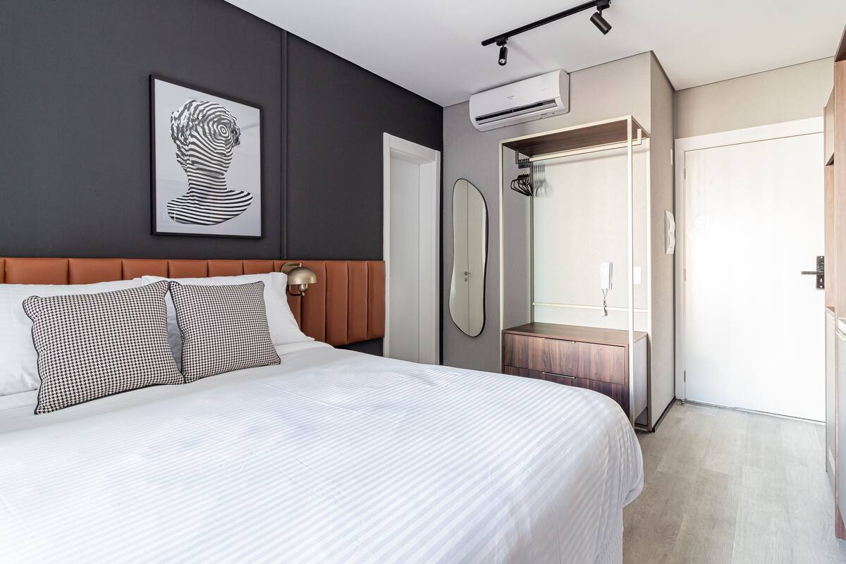 A bedroom with a bed, a headboard, a wall-mounted air conditioner, a mirror, and a wardrobe.