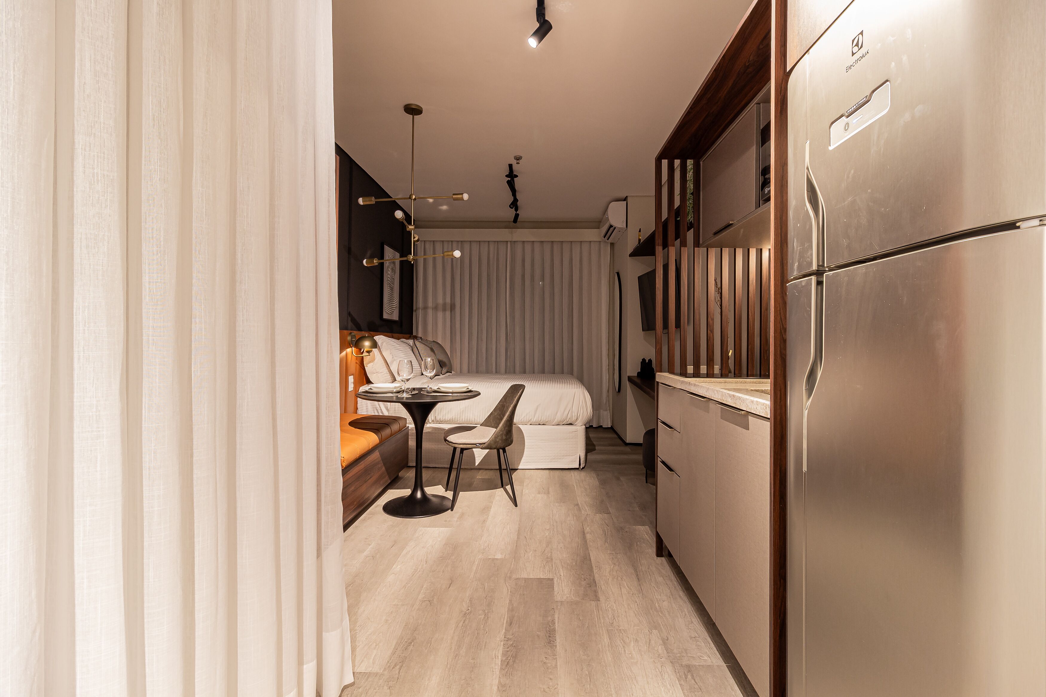 Cocina compacta con refrigerador, una mesa de comedor con sillas y una cama al fondo.