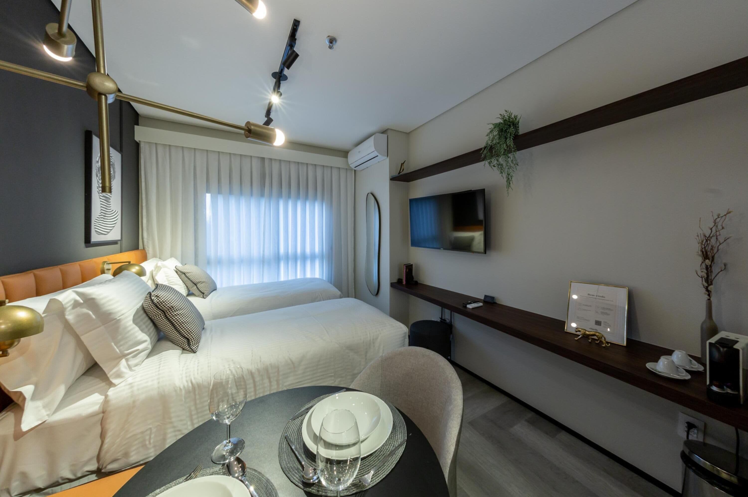 A hotel room with a bed, bedside table, and a dining area with a table set for two.