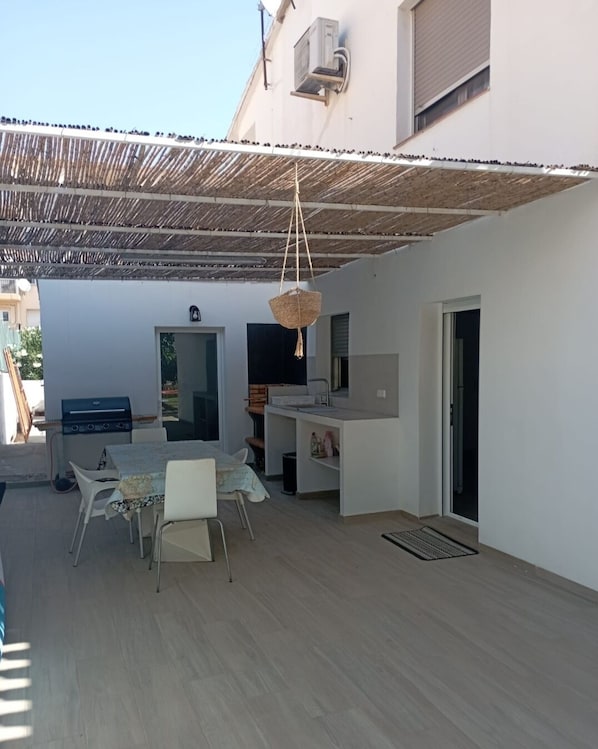 A covered outdoor patio with a dining table and chairs, a hanging light fixture, and a grill.