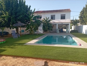 A house with a swimming pool, surrounded by a well-maintained lawn and some trees.