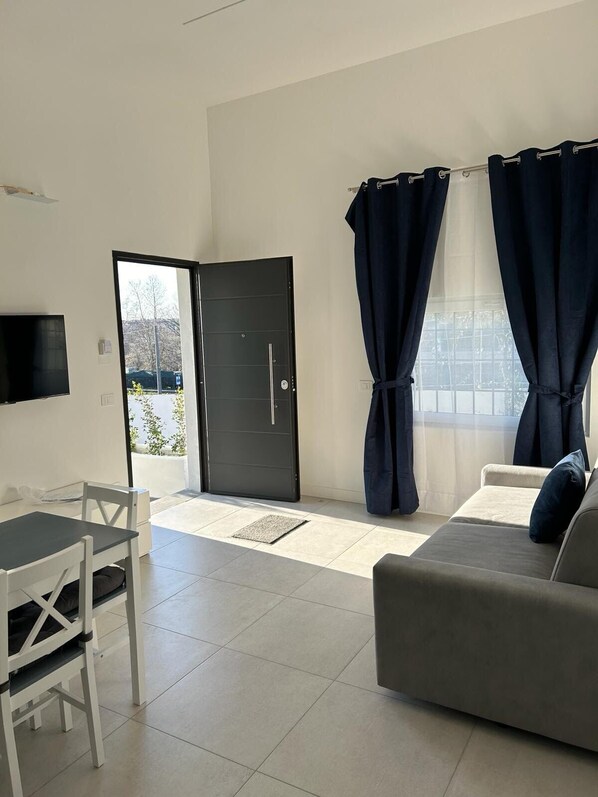 Un salon moderne avec un canapé, une table à manger et des chaises, ainsi qu’une porte noire donnant sur l’extérieur.