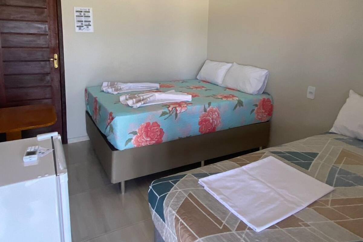 A small, clean room with a bed, a desk, and a refrigerator.
