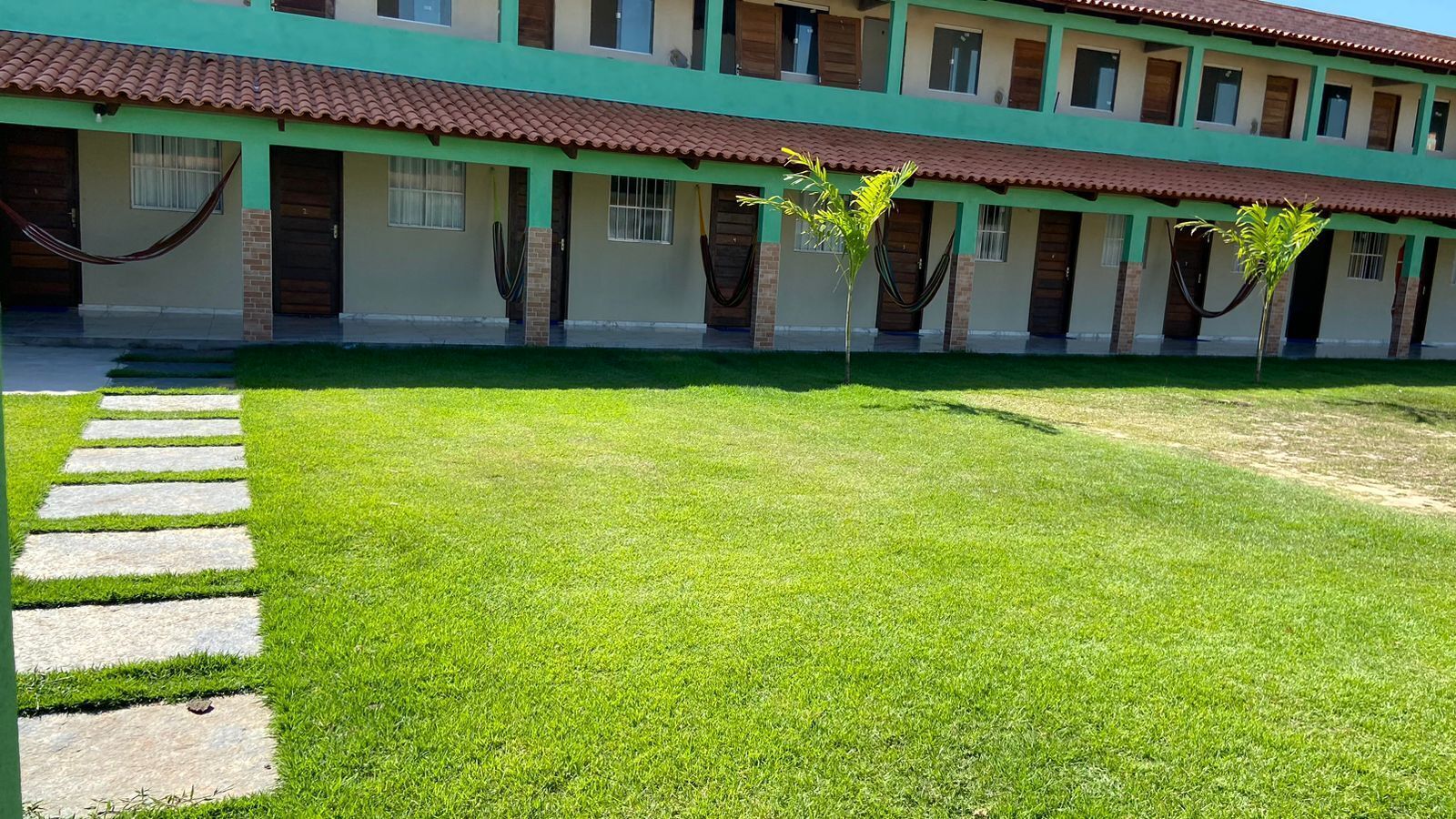 Un edificio con fachada verde y techo de tejas. Hay un área con césped y un camino de piedra que lleva al edificio.