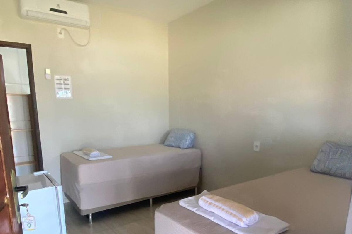 A small, clean room with two beds, a refrigerator, and a ceiling air conditioner.