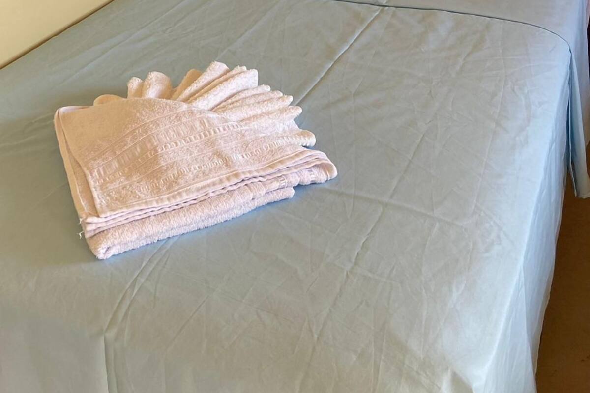 A single bed with a light blue bedspread and a folded towel on it.