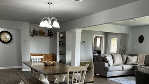 A dining area with a wooden table and benches, a white chair, and a chandelier. - Cozy Southern Charm in Houma (Houma)