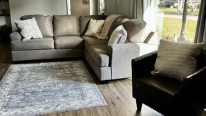 A living room with a sectional sofa, a small armchair, a blue rug, and a wooden floor. - Cozy Southern Charm in Houma (Houma)