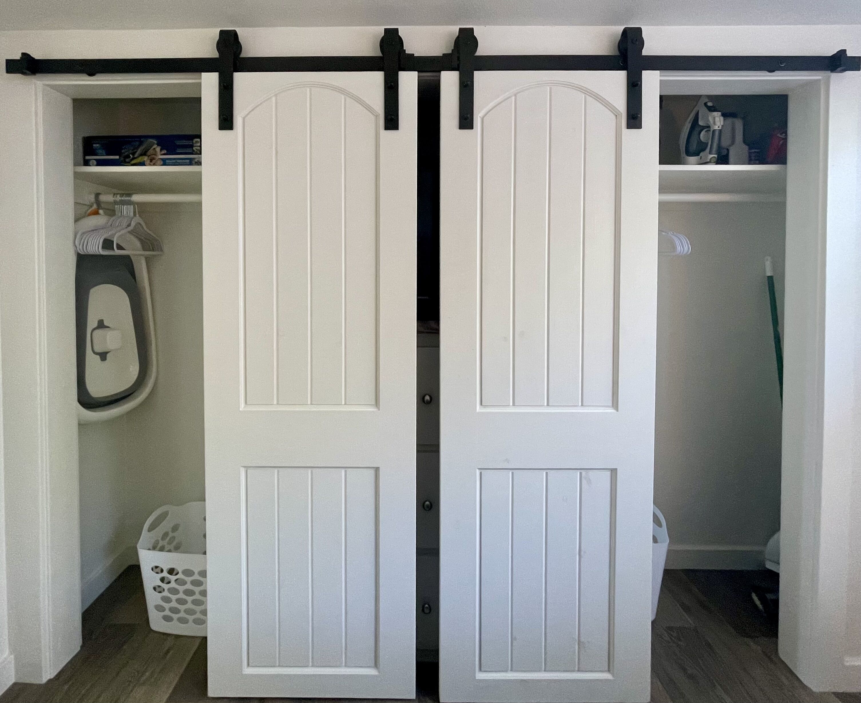 A white sliding door with a black track, leading to a closet with shelves and a hanging rack.
